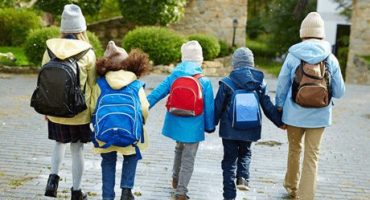 cinco crianças jovens caminham de mãos dadas agasalhadas e mochila nas costas