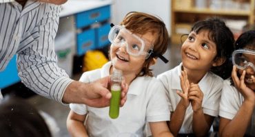 3 crianças sorriem e olham para professor enquanto ele mostra tudo de ensaio com líquido verde