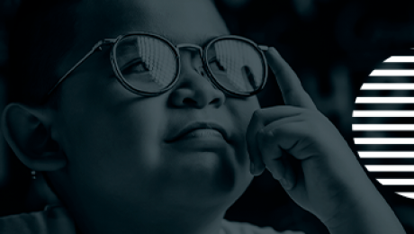 criança aponta dedo indicador nos seus óculos e olha para cima.