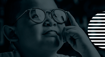 criança aponta dedo indicador nos seus óculos e olha para cima.