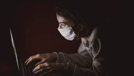 pessoa com máscara de proteção usa computador portátil na penumbra