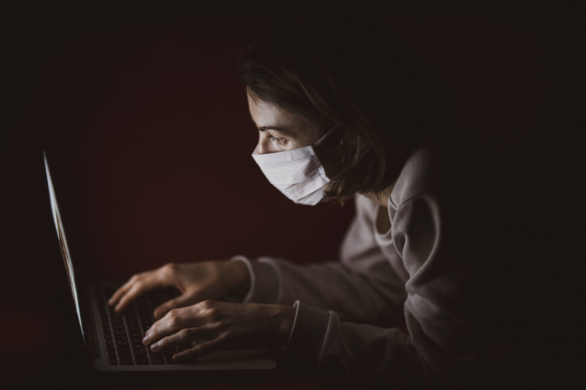 pessoa com máscara de proteção usa computador portátil na penumbra