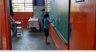 duas crianças na sala de aula escrevendo no quadro verde