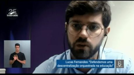 Print de tela videoconferência mostra homem branco de barba e óculos de grau falando. No canto inferior esquerdo, intérprete de LIBRAS.