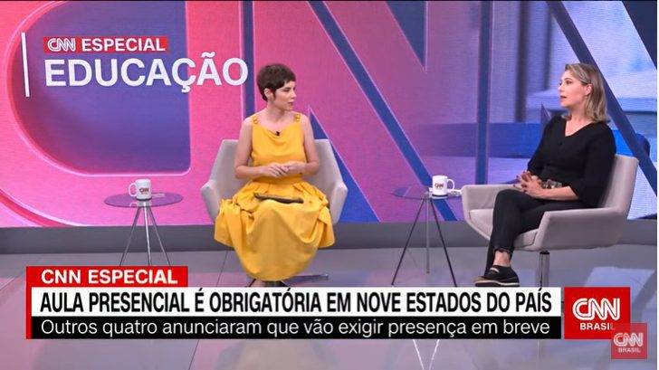 Print de tela exibição CNN Especial Educação. Duas mulheres sentadas conversando. Uma usa um vestido amarelo, tem cabelos curtos. Outra, veste calça e blusa pretas, tem cabelos louros.