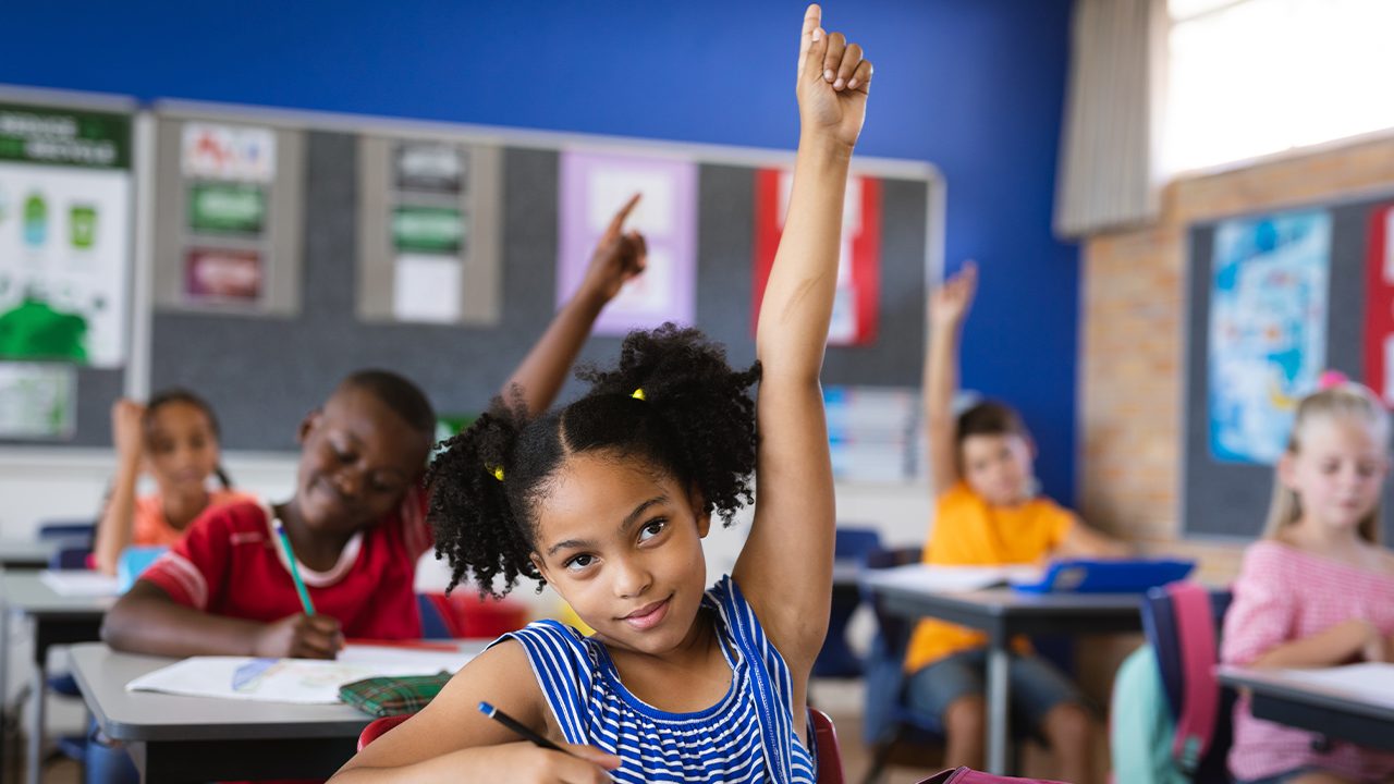 Menina negra levanta a mão para fazer pergunta numa sala de aula
