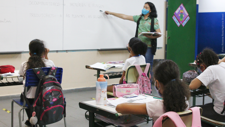 Em sala, professora em pé na frente de alunos aponta para lousa. Foto: Rovena Rosa. Agência Brasil.