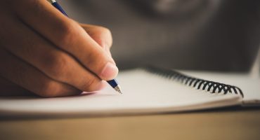 Foto desfalcada de um caderno e uma mão segurando uma caneta