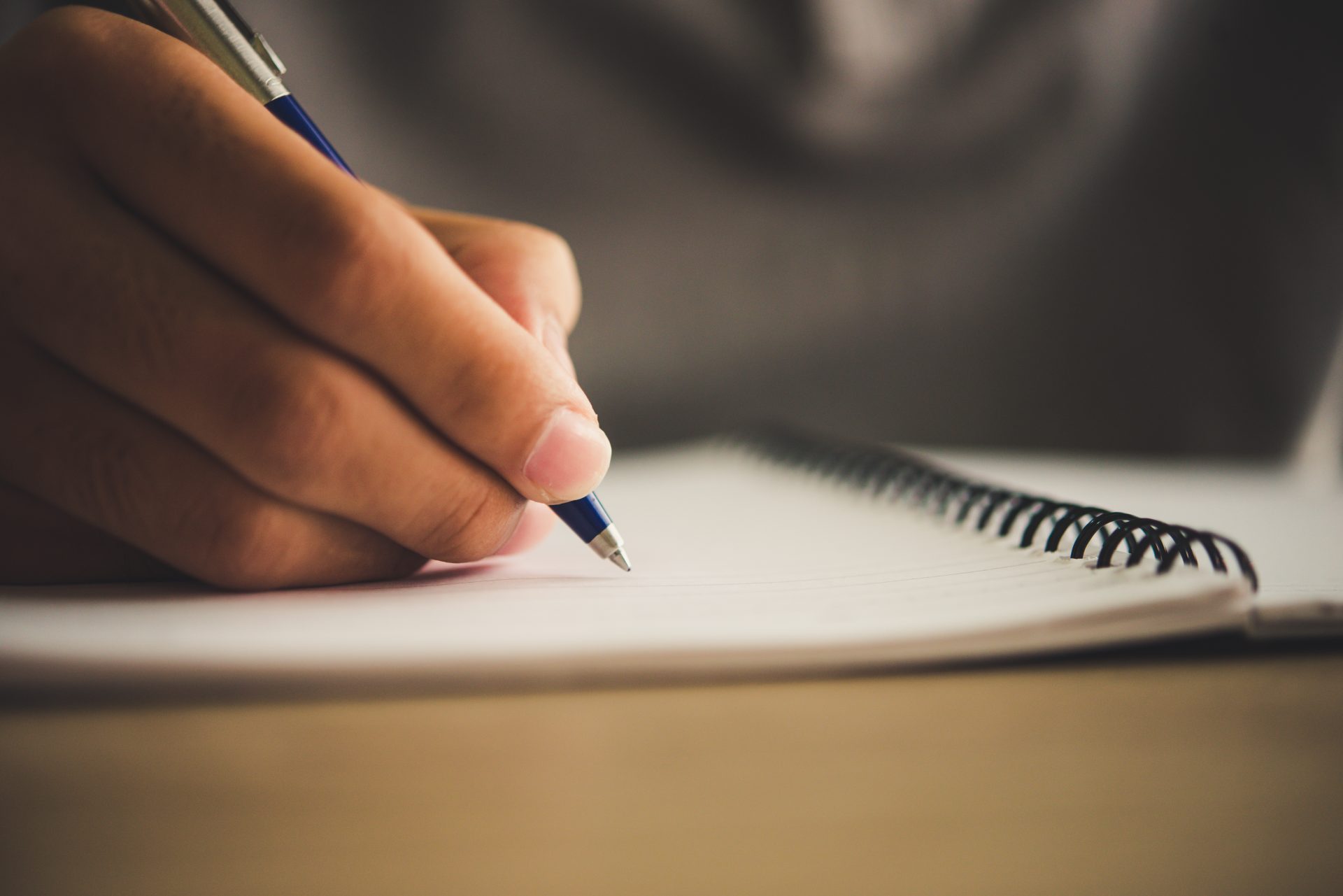 Foto desfalcada de um caderno e uma mão segurando uma caneta