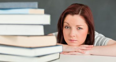 Uma mulher ruiva olhando para a foto com uma pilha de livros desfocada em sua frente