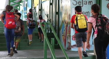 Jovens e crianças, de costas, sobem escadas de uma escola