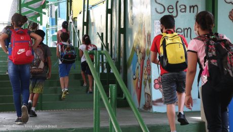Jovens e crianças, de costas, sobem escadas de uma escola