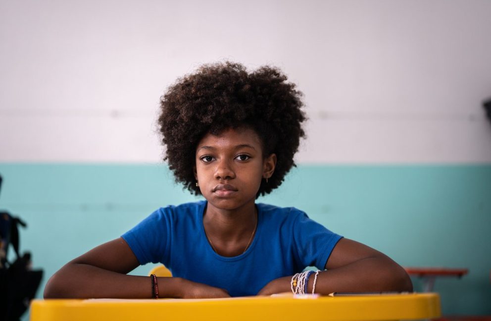 Criança negra sentada em sala de aula