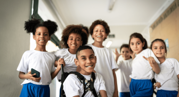 Seis crianças de uniforme branco e azul posando para a foto no corredor da escola.