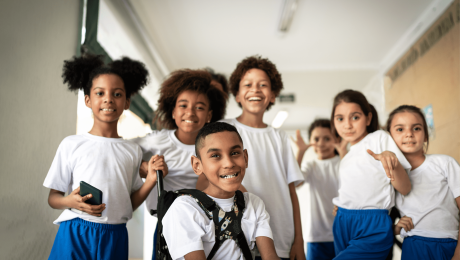 Seis crianças de uniforme branco e azul posando para a foto no corredor da escola.