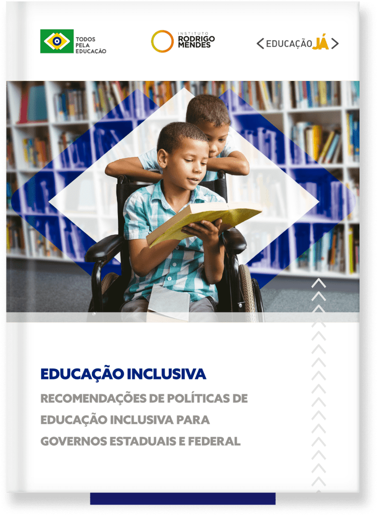 Menino em uma cadeira de rodas segura e olhra pra livro junto com outro garoto, que está detrás da cadeira