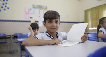 garoto sentado à carteira em sala de aula aponta algo no livro