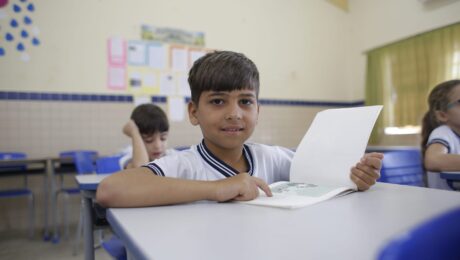 garoto sentado à carteira em sala de aula aponta algo no livro