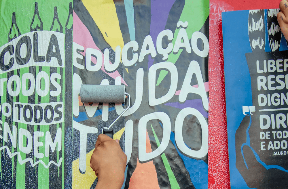 mão infantil passa um rolo sobre um lambe-lambe com frase: educação muda tudo