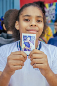 criança negra de cabelos crespos sorri e mostra sua foto tipo polaroid