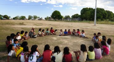 crianças indigenas sentadas no chão da aldeia