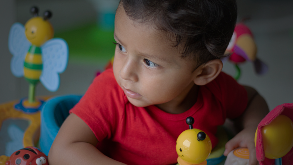 bebê pardo de cerca de 1 ano de idade, de cabelos castanhos curtos, olha pro lado esquerdo