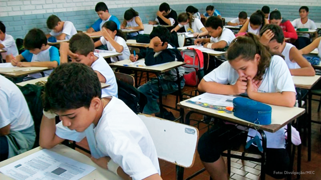 sala de aula com várias crianças sentadas olhando para o livro sobre a carteira