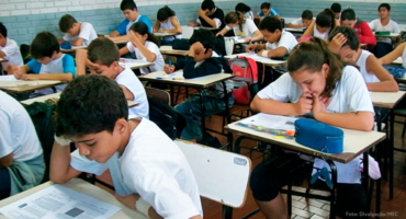 sala de aula com várias crianças sentadas olhando para o livro sobre a carteira