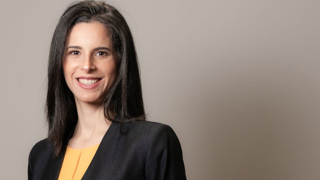 Mariana Luz, CEO da Fundação Maria Cecilia Souto Vidigal é uma mulher de cabelos lisos e escuros, na altura dos ombros, sorri para a câmera em um retrato profissional. Ela veste blazer preto sobre uma blusa amarela. O fundo é neutro, em tom bege claro, destacando a figura em primeiro plano.