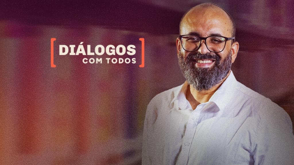 Diálogos com Todos: Diálogos com Todos Helton Souto Lima. A imagem mostra Helton Souto Lima, um homem sorridente, de barba e óculos, vestido com camisa branca. Ele está posicionado à direita sobre um fundo desfocado em tons quentes. À esquerda, aparece o título “Diálogos com Todos” entre colchetes em laranja.